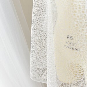 May include: White lace fabric with a delicate, circular pattern. The fabric is sheer and lightweight, making it ideal for a variety of crafting projects.