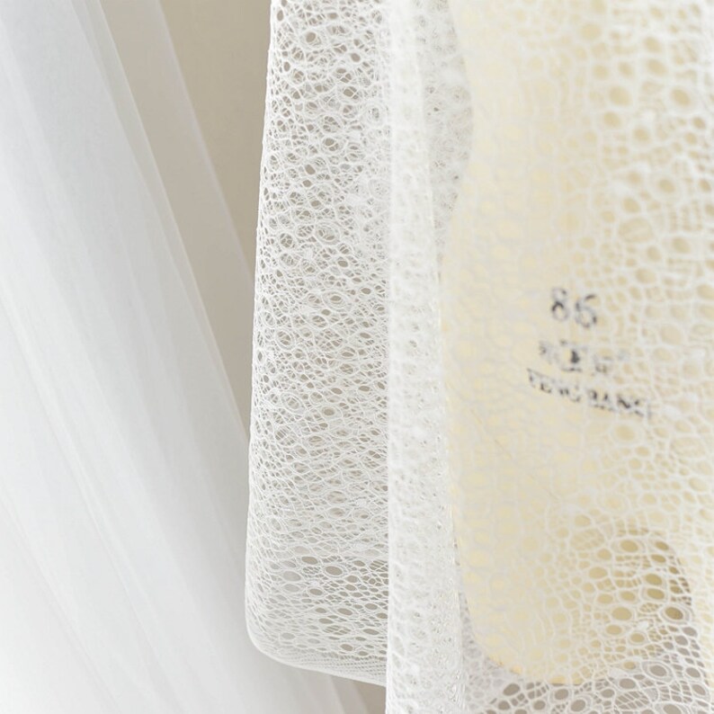 May include: White lace fabric with a delicate, circular pattern. The fabric is sheer and lightweight, making it ideal for a variety of crafting projects.