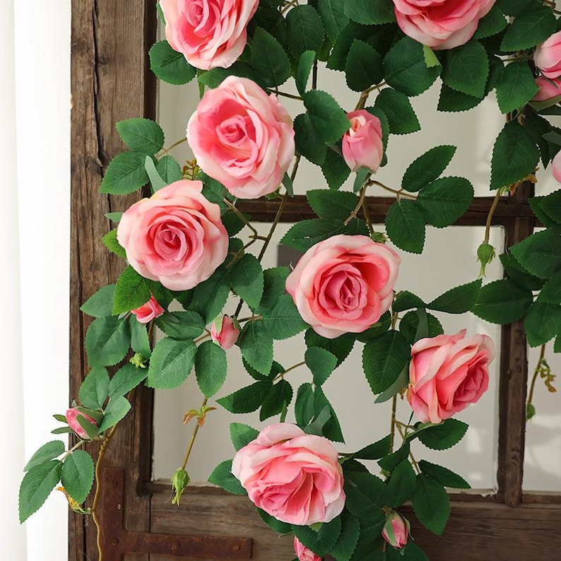 May include: A close-up of a climbing rose arrangement with large, open pink roses and green leaves. Several rose buds are also visible. The roses are arranged on a dark wooden background.