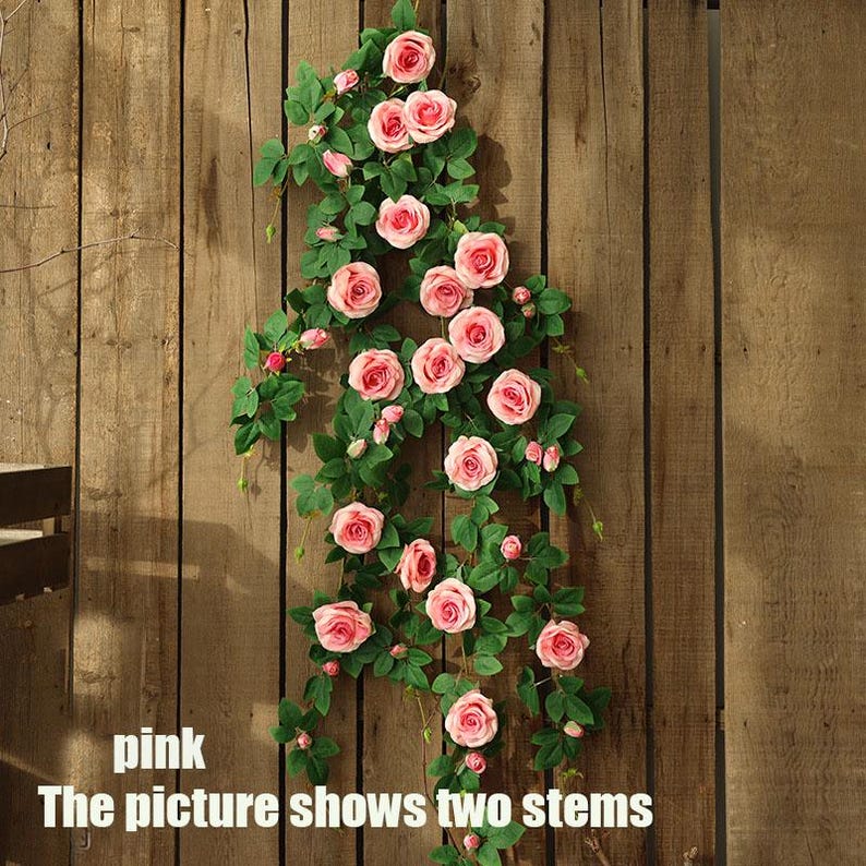 May include: Two stems of artificial pink roses with green leaves cascade down a wooden plank background. The image text reads "pink" and "The picture shows two stems".