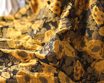May include: Close-up of a black fabric with a gold floral pattern. The fabric is textured and has a luxurious feel.
