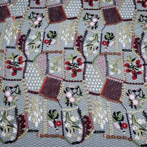 Puede incluir: Primer plano de una tela gris con un patr&oacute;n repetido de flores bordadas y formas geom&eacute;tricas en tonos rojos, burdeos, verdes y blancos.