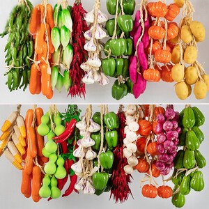 Pu&ograve; includere: Assortimento di verdure e frutta artificiali appese a delle corde. Le verdure includono peperoni verdi, peperoncini rossi, aglio, cipolle verdi e carote. La frutta include zucche rosse e arancioni e patate.