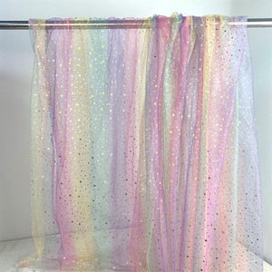 Könnte beinhalten: Ein transparenter, leichter Stoffvorhang mit einem vertikalen Regenbogenverlauf in Pastellfarben wie Rosa, Gelb, Blau und Violett. Das durchscheinende Material ist mit einem sich wiederholenden Muster aus kleinen, metallisch goldenen Sternen verziert.