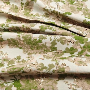 May include: Close-up of a white fabric with a green and gold floral pattern. The fabric has a textured, embossed look.