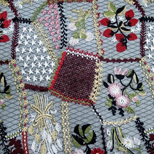Puede incluir: Primer plano de una tela bordada en blanco y negro con un dise&ntilde;o de patchwork. La tela presenta varios patrones florales y geom&eacute;tricos en tonos rojos, rosas, verdes y dorados.
