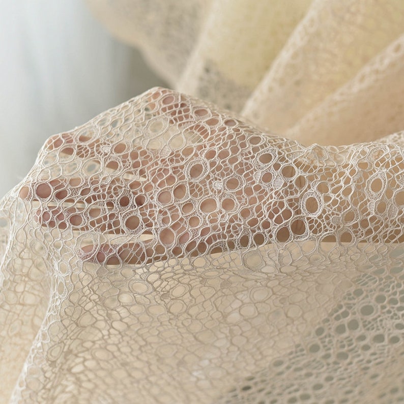 May include: Beige lace fabric with a delicate circular pattern. The fabric is soft and sheer, with a subtle shimmer.