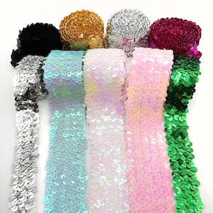 Puede incluir: Una colección de adornos de lentejuelas en varios colores, incluyendo negro, dorado, plateado y rosa. El adorno está dispuesto en rollos y tiras, mostrando la calidad brillante y reflectante de las lentejuelas. Ideal para manualidades y adornos.