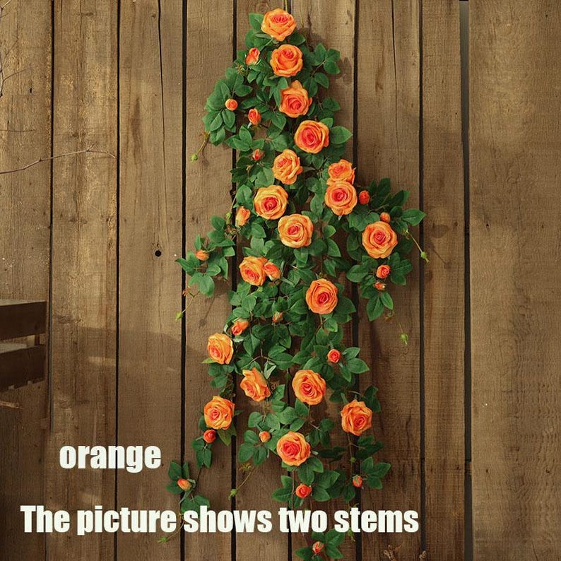May include: Two artificial rose vines with orange blooms and green leaves cascade down a wooden background. The text "orange" and "The picture shows two stems" are visible at the bottom of the image. The roses are in various stages of bloom.
