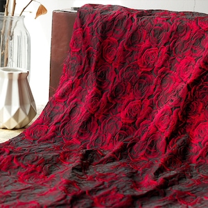 Puede incluir: Tela roja con un patrón en relieve de rosas rojas. La tela tiene un fondo oscuro, casi negro.