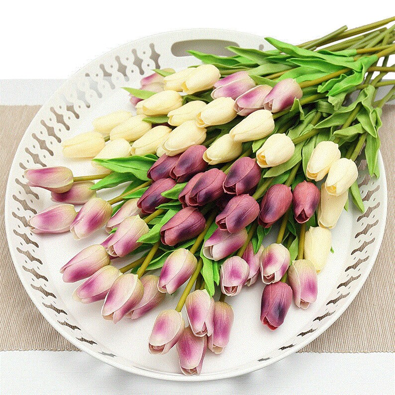 Op de afbeelding: Een boeket kunstmatige tulpen in cr&egrave;me, paars en roze tinten. De tulpen zijn gerangschikt in een wit decoratief dienblad.