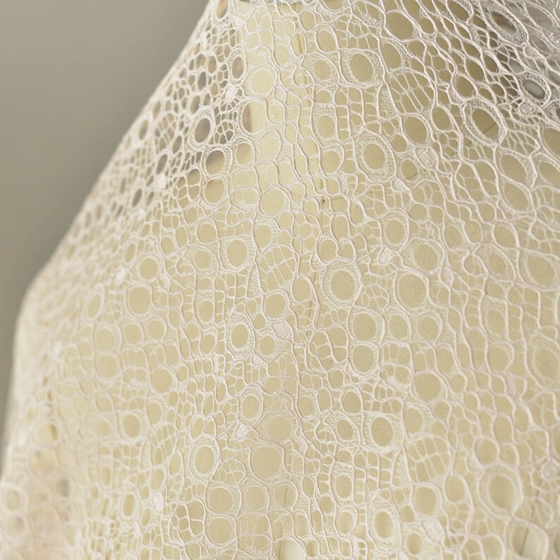 May include: White lace fabric with a delicate, intricate pattern of small circles and lines. The lace has a soft, airy feel and would be perfect for a variety of crafting projects.
