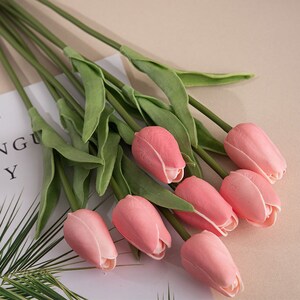 Op de afbeelding: Een boeket van roze kunstmatige tulpen met groene stelen en bladeren.