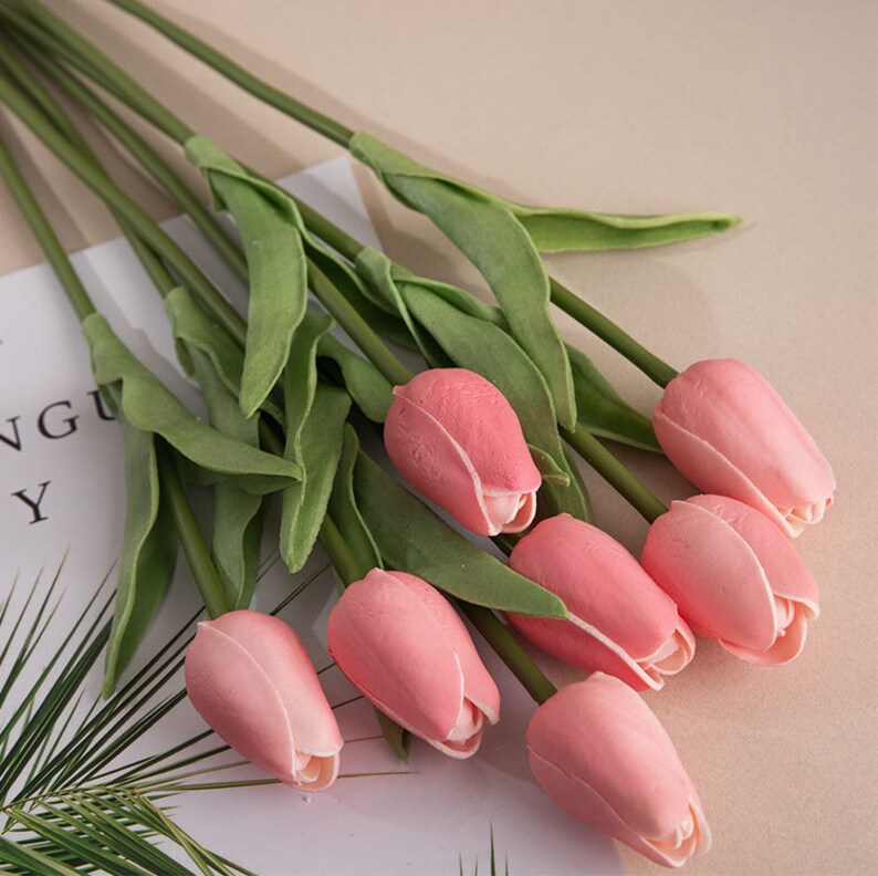 Op de afbeelding: Een boeket van roze kunstmatige tulpen met groene stelen en bladeren.