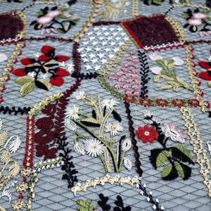 Puede incluir: Primer plano de una tela delicada bordada con un dise&ntilde;o de patchwork. La tela presenta una variedad de motivos florales en tonos rojos, rosas, verdes y blancos, sobre un fondo de malla negra.