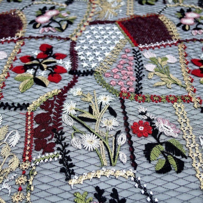 Puede incluir: Primer plano de una tela delicada bordada con un dise&ntilde;o de patchwork. La tela presenta una variedad de motivos florales en tonos rojos, rosas, verdes y blancos, sobre un fondo de malla negra.