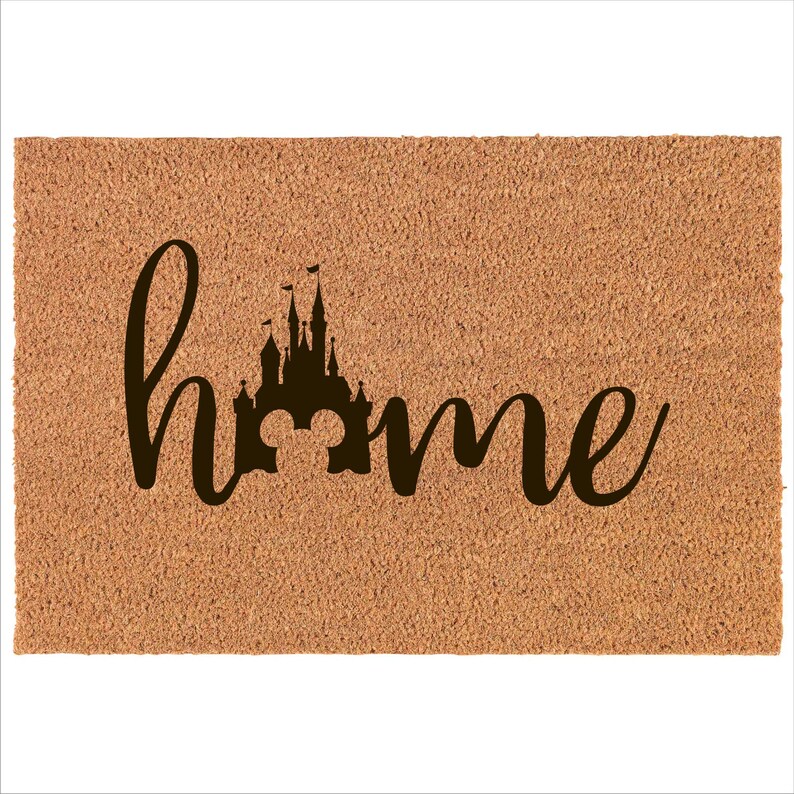May include: A brown coir doormat with the word "home" written in black cursive script. The letter "o" in the word "home" is replaced with a silhouette of the Cinderella Castle from Disney World.