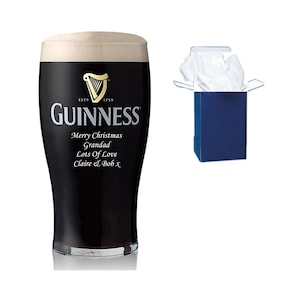 May include: A personalized Guinness pint glass with a black and gold logo and the text "ESTD 1759 GUINNESS Merry Christmas Grandad Lots of Love Claire & Bob x". The glass is sitting on a white surface and is in a blue gift box.