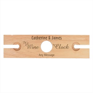May include: Wooden wine bottle holder with two slots for glasses. It says "It's Wine 'Clock" and "Catherine & James" with space for a personalized message.