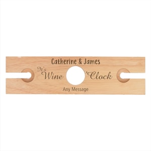 May include: Wooden wine bottle holder with two slots for glasses. It says "It's Wine 'Clock" and "Catherine & James" with space for a personalized message.