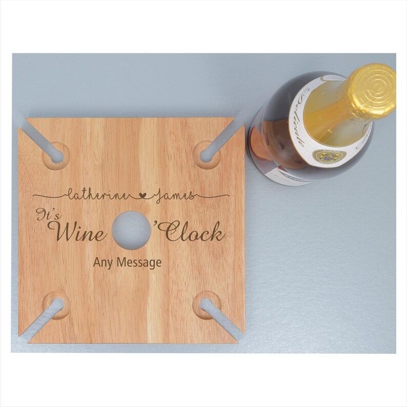 May include: Wooden wine rack with four slots for glasses and a bottle. It has the text "It's Wine 'Clock" and "Catherine & James" engraved on it.