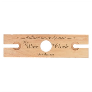 May include: Wooden wine bottle holder with two slots for glasses. It has the text "It's Wine 'Clock" and "Catherine & James" engraved on it.