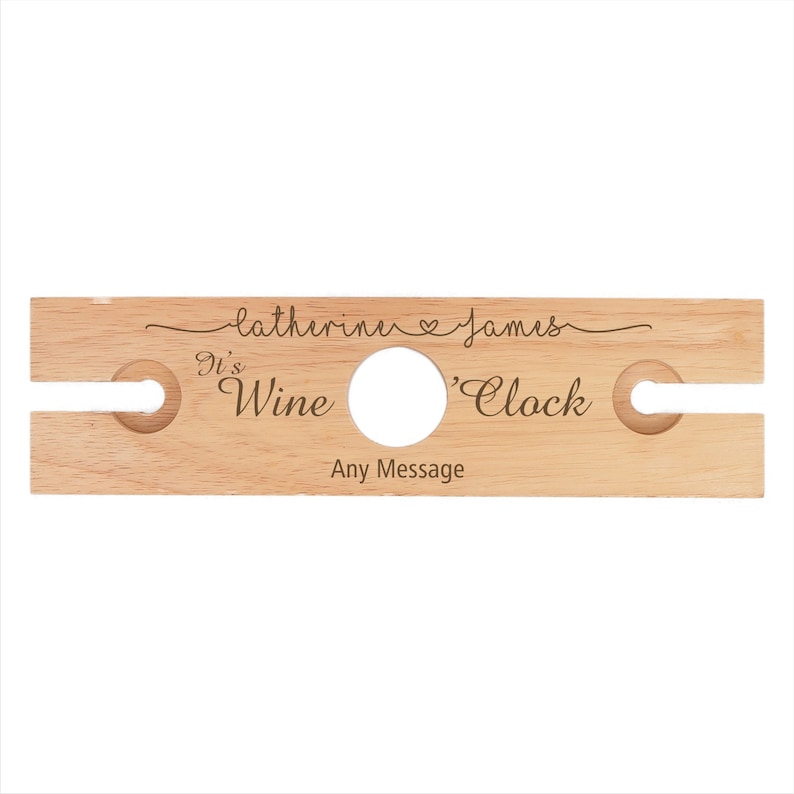 May include: Wooden wine bottle holder with two slots for glasses. It has the text "It's Wine 'Clock" and "Catherine & James" engraved on it.