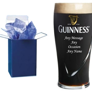 May include: A personalized Guinness pint glass in a blue gift box. The glass has the Guinness logo and the text "ESTD 1759 GUINNESS" printed on it. The text "Any Message Any Occasion Any Name" is also printed on the glass.