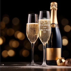 Puede incluir: Dos copas de champán con un mensaje personalizado grabado en el vidrio. El mensaje dice "Chloé 21 & Fabulous Love Craig & Nicola xxx". Una botella de champán está en el fondo.