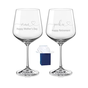 May include: Two clear glass wine glasses with stems. The left glass features the text nan with a heart and Happy Mother's Day. The right glass features the text jackie with a heart and Happy Retirement. A small blue gift box with white tissue paper is centred between them.