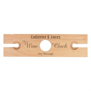 May include: Wooden wine bottle holder with two slots for glasses. It says "It's Wine 'Clock" and "Catherine & James" with space for a personalized message.