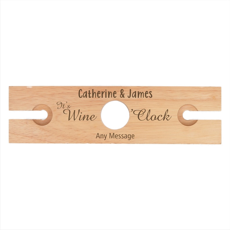 May include: Wooden wine bottle holder with two slots for glasses. It says "It's Wine 'Clock" and "Catherine & James" with space for a personalized message.