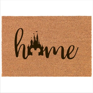 May include: A brown coir doormat with the word "home" written in black cursive script. The letter "o" in the word "home" is replaced with a silhouette of the Cinderella Castle from Disney World.