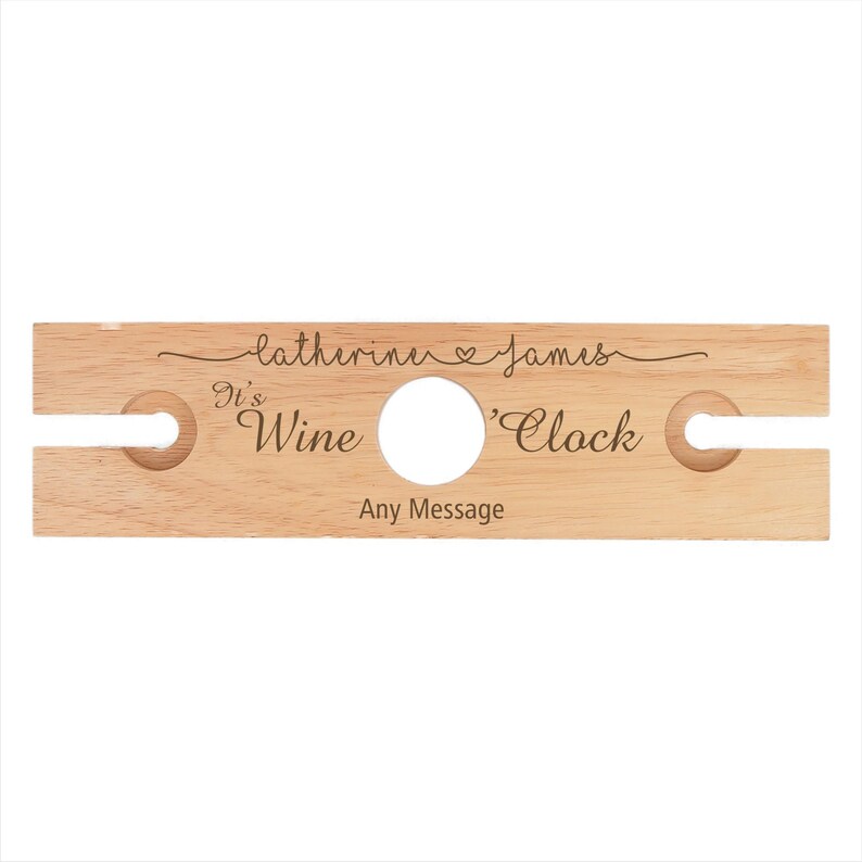 May include: Personalized wooden wine bottle holder with two slots for glasses. It reads "It's Wine 'Clock" and "Catherine & James" with a heart symbol.
