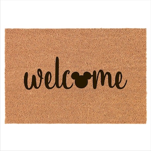 May include: A brown coir doormat with the word "welcome" in black cursive lettering and a black Mickey Mouse silhouette in the middle of the word.