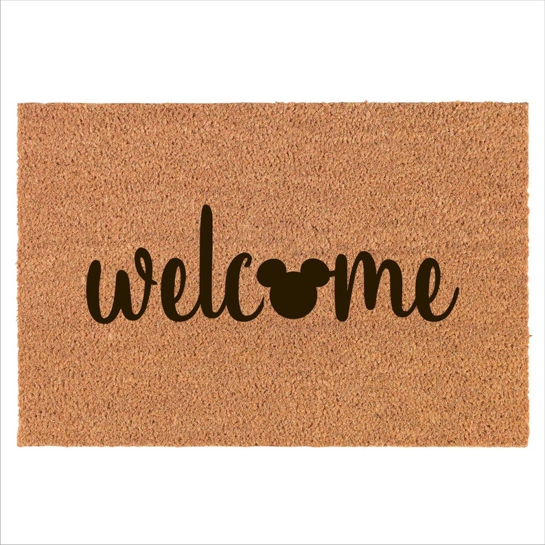 May include: A brown coir doormat with the word "welcome" in black cursive lettering and a black Mickey Mouse silhouette in the middle of the word.