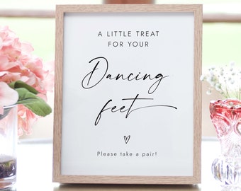 Op de afbeelding: Een ingelijst bord met de tekst "A LITTLE TREAT FOR YOUR Dancing feet Please take a pair!" in zwart schrift. De lijst is lichtbruin. Roze bloemen staan in een vaas links en een decoratieve glazen vaas rechts.