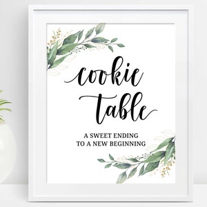 May include: White framed sign with the words "cookie table" in elegant script. The sign includes the phrase "A sweet ending to a new beginning" and is decorated with green and gold floral accents.