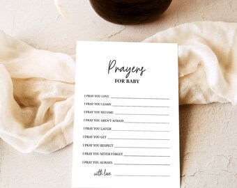 May include: A white card featuring the words "Prayers FOR BABY" in a stylish script. The card is designed for writing prayers, with prompts such as "I pray you learn" and "with love" at the bottom. A dark brown object and a cream-colored cloth are in the background.