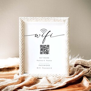 May include: White framed sign with the word "wifi" in cursive script, a black and white QR code, and the text "NETWORK Network Name PASSWORD Wifi Password".