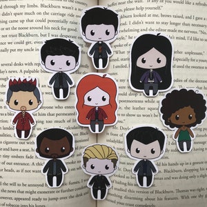 May include: A collection of ten chibi-style character stickers. Each sticker features a unique character design with large eyes and simplified features. The characters are dressed in various outfits, with a range of hair colors and styles. The stickers are arranged on a book page.