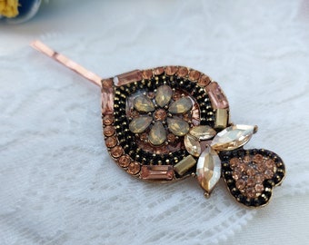 May include: A gold hair clip with a floral design and clear and amber rhinestones.