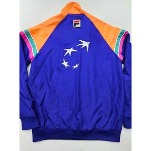 Peut inclure: Veste bleue vintage avec des accents orange et roses. La veste pr&eacute;sente un motif d'&eacute;toiles blanches au dos et le logo de la marque sur la poitrine. La veste a une fermeture &eacute;clair compl&egrave;te et un ourlet et des poignets c&ocirc;tel&eacute;s.