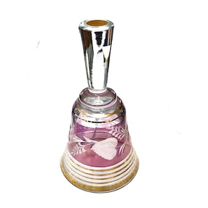 May include: A pink glass bell with a clear glass handle. The bell is decorated with etched white floral designs and gold trim.