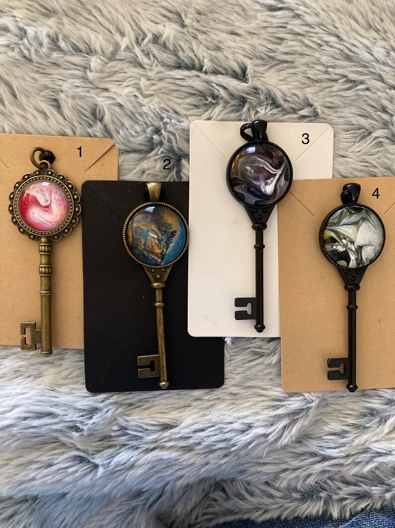 May include: Four key-shaped pendants with different abstract designs. Each pendant is made of metal and has a glass cabochon with a unique swirl pattern. The pendants are numbered 1 through 4.