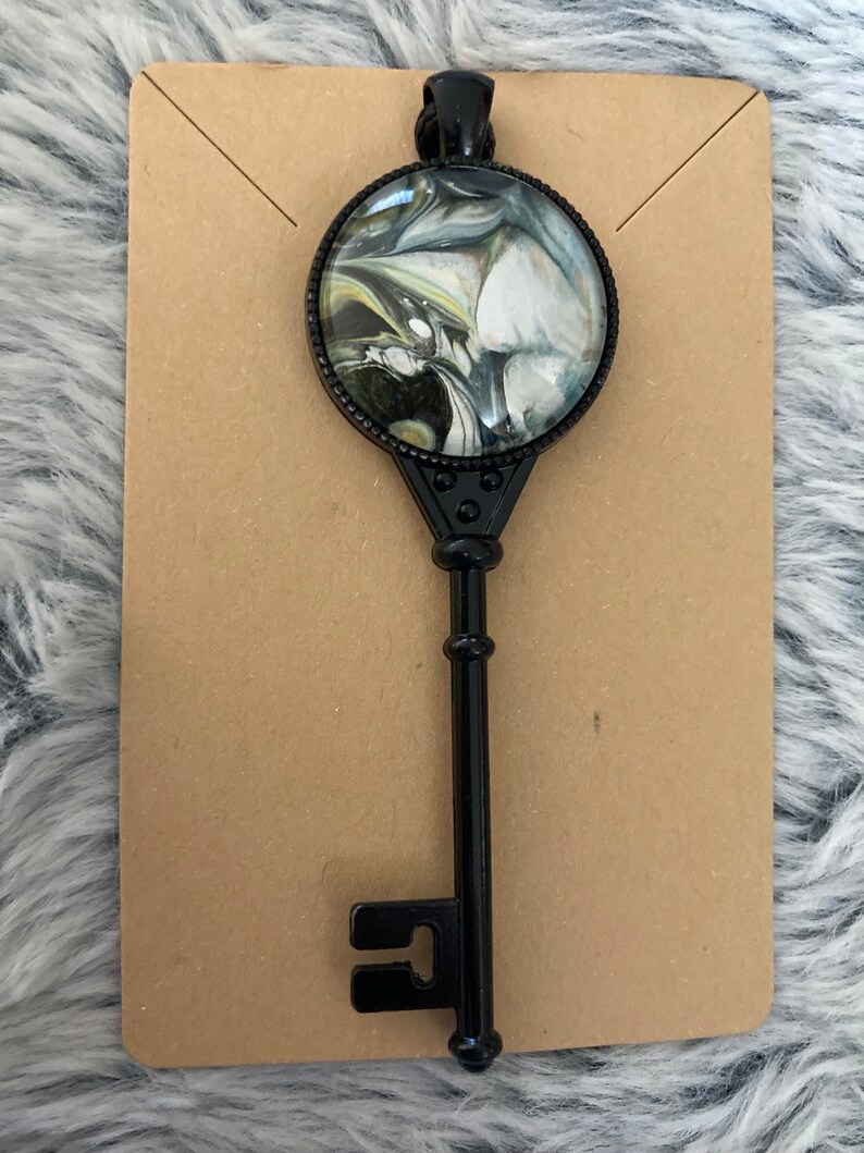 May include: A black metal key pendant with a round glass charm featuring a swirling black, white, and green marble design.