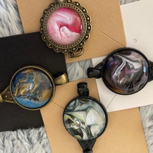 May include: Four key-shaped pendants with round glass cabochons featuring abstract swirl designs in pink, blue, black, and white.