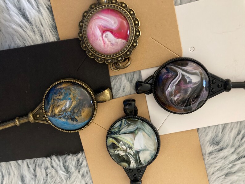May include: Four key-shaped pendants with round glass cabochons featuring abstract swirl designs in pink, blue, black, and white.