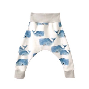May include: White baby pants with a blue whale print. The pants have a grey elastic waistband and cuffs.
