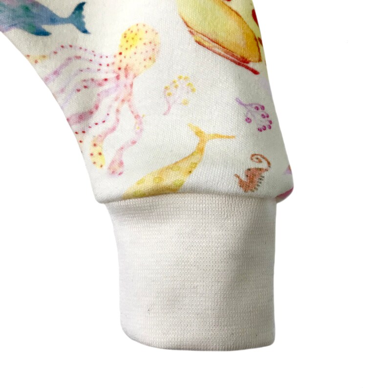 May include: Close-up of the cuff of a white long-sleeved shirt with a colorful underwater print featuring sea creatures like an octopus, fish, and seahorses.